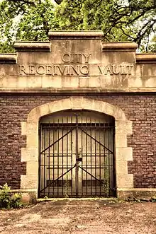 Brick and stone arched door with iron gate, sign above says CITY RECEIVING VAULT.