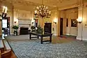 A large carpeted lobby with a center table, fireplace, and chandelier