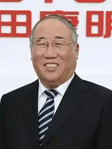 a smiling man who is bald, wearing glasses, a white shirt, a suit and a black tie with blue stripes