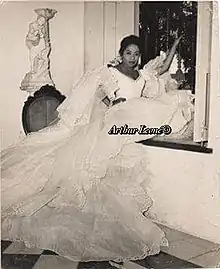 A young woman of color wearing a large white dress, sitting in a window well