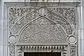 An intricately carved marble tympanum above an exterior window of the mosque
