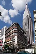 In the foreground: the abandoned Yoyogi Kaikan [ja] building that appears in the film. The demolition of the building was completed in January 2020 and it no longer exists. Note that the rooftop shrine in this film is fictional. Back: the NTT DoCoMo Yoyogi Building (Docomo Tower), which frequently appears in Shinkai's films.