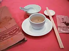 A ceramic spoon in a bowl, pair of chopsticks, plate, and cup of tea
