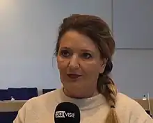 A Caucasian woman with dark-blond braided hair in a white room