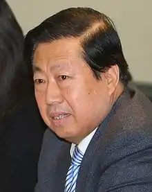 a man with a wavy haircut, wearing white shirt, a grey suit and a blue tie
