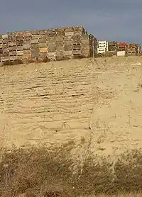  This photo shows a canyon cut into the surrounding flat soil with over 20 distinct horizontal layers of sediment, each clearly demarked from the layer below. Above the canyon lip a number of boxes used for transporting harvested apples are stacked; the size of these boxes indicates that the layers each are 0.5–1 meter in depth.