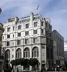 An Edwardian building with six floors stands on a moderate day, a flag flying atop it.