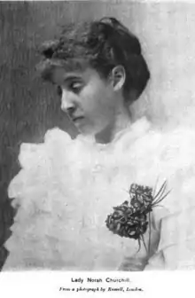 A young white woman wearing a very ruffled white dress or blouse; her hair is dressed in a chignon, with curly fringe