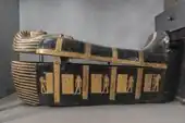 Side view of black and gold coffin shaped like a mummy