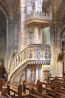 Photo d'une colonne d'église sur laquelle a été construite une chaire en pierre blanche. Elle repose sur deux colonnettes et est accessible par un escalier qui entoure la colonne. Un baldaquin surmonte l'ensemble.