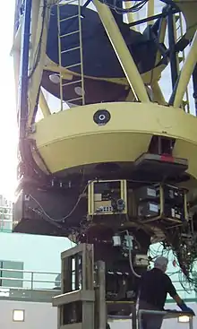 A very large, hollow metal framed cylindrical structure pointing straight up with a man standing underneath working on the many electronic components at the bottom.