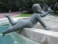Imagen de un angelote en piedra, desnudo tumbado sobre su vientre en el borde de una fuente