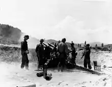 A large artillery gun fires as several soldiers look on