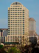 The building is generally light brown. The lower portion of the tower is a vertical rectangle, followed by a setback and then a semi-circle.