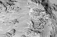 Abanicos aluviales en el cráter Mojave, vistos por HiRISE. El terreno alto está a la derecha. La red ramificada de canales se extiende desde un terreno más alto (borde del cráter) hasta un terreno más bajo.