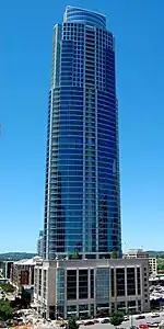 Slightly elevated view of a 60-story skyscraper with a glass facade set atop a rectangular pedestal; the building has balconies on every floor and has two small setbacks near the roofline.