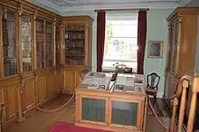 Photograph of a laboratory, with glass-encased, wooden bookcases on two walls and a window on the third. There is a display case in the middle of the room.