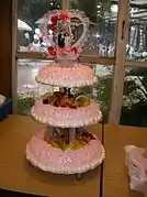 Un pastel de bodas de tres pisos, con decoración de frutas en los pisos inferiores y coronado con figuritas en el superior.