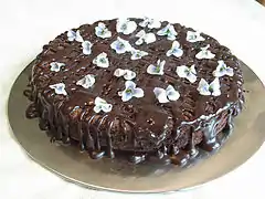 Un pastel de chocolate cubierto con ganash y adornado con violetas.