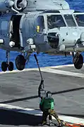 Marineros de la Armada de Estados Unidos enganchan un cable de carga a un helicóptero Sikorsky SH-60 Seahawk asignado al Escuadrón de Helicópteros Anti-Submarinos 4 durante una maniobra de reabastecimiento vertical en el Océano Pacífico el 16 de julio de 2010.