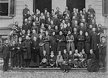 Fotografía en blanco y negro de un grupo de cerca de 90 personas.
