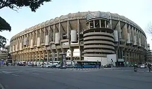Vistas del Estadio Santiago Bernabéu en medio de una calle con coches y semáforos.