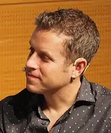 A man with brown hair smiling while facing to the left of the camera.