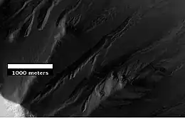 Barrancos en el cráter Ross, visto por HiRISE bajo el programa HiWish. Debido a que los barrancos están en el borde estrecho de un cráter y comienzan a diferentes alturas, este ejemplo no es consistente con el modelo de barrancos causado por los acuíferos.