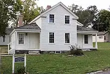 Fotografía a color de una casa blanca de dos pisos con dos cobertizos laterales.