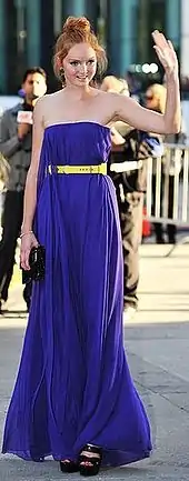 Cole outside wearing a strapless purple dress with her hair up in a large bun, surrounded by photographers.