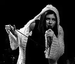 A black-and-white photograph of Marina and the Diamonds performing live while wearing a hooded cardigan.