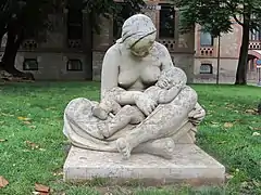 Escultura en piedra que representa una mujer con el pecho desnudo, sentada en el suelo con las piernas cruzadas y un niño en los brazos