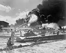Marineros junto a aviones siniestrados, al fondo, explosión del USS Shaw.