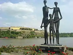 Au bord d'un fleuve, un monument composé de trois statues représentant des silhouettes émaciées.