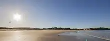 Playa Grande de Miño con sol, donde a la derecha se ve el mar, que está en marea baja, y a la izquierda el sol y la playa.