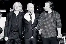 Una foto en blanco y negro de los miembros de R.E.M. abrazando y sonriendo en el escenario