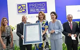 Pablo Gómez Borbón recibe de manos de la señora Milagros Germán, ministra de Cultura, el diploma correspondiente al Premio Nacional Feria del Libro Eduardo León Jimenes 2022. Observan las señoras María Amalia León, presidenta de la Fundación Eduardo León Jimenes, y Carolina Mejía, alcaldesa de Santo Domingo.