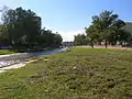 El río Suquía en su paso por el corazón de la ciudad argentina de Córdoba; notar que su caudal está muy reducido, dejando un amplio cauce cubierto de hierbas.