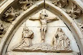 Dintel labrado en la portada oeste: un cristo en el centro, una virgen sedente con niño a un lado y la figura de un abad arrodillado al otro.