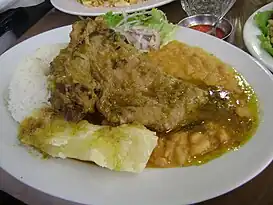 Seco de cabrito acompañado de yucas cocidas, arroz blanco, frejoles y salsa criolla