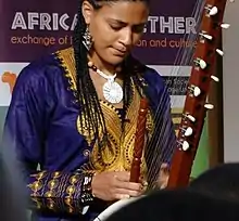 Une femme à la peau brune et claire, portant de fines nattes africaines lui tombant sur les épaules, joue en fermant les yeux de la kora. Derrière, on peut lire sur une affiche "Africa Together".