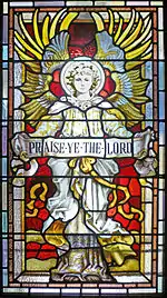 La imagen en el vitral es de un ángel con sus alas estiradas detrás y sosteniendo una bandera que dice "Praice Ye the Lord" (Adorad al Señor)