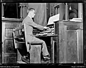 Una foto en blanco y negro de un hombre tocando el órgano mostrando el teclado y los pedales.