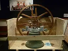 Foto de una grande campana de metal y su soporte circular de madera en una caja medio abierta