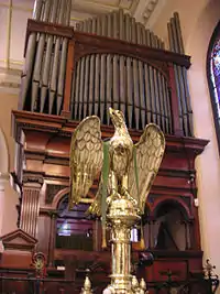 El atril de bronce está en su tradicional forma de águila y los tubos del órganp detrás