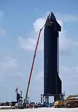 Fotografía de un trabajador en una plataforma de trabajo aérea que repara el escudo térmico negro de una nave espacial