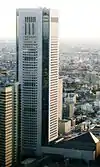 Aerial view of a white, window-dotted, rectangular high-rise; the corners are cut and made of glass