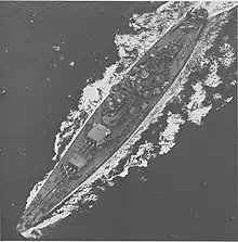 A large battleship steams through choppy seas. Three floatplanes are located on the stern.