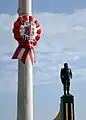 Escarapela de plástico con la frase “¡Feliz 28 de Julio!” colgada en un poste al costado de la estatua de José Quiñones.