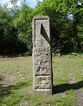 A standing stone in a grassy field surrounded by trees. The stone contains a vertical sundial centered on 1 o'clock, and is inscribed "HORAS NON NUMERO NISI ÆSTIVAS" and "SUMMER TIME ACT 1925"
